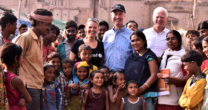 A group photo of smiling adults and children outdoors in a village setting.